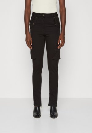 Widok z przodu osoby noszącej czarne wąskie spodnie typu cargo z zipami w pobliżu kostek oraz czarne botki na kostkę.