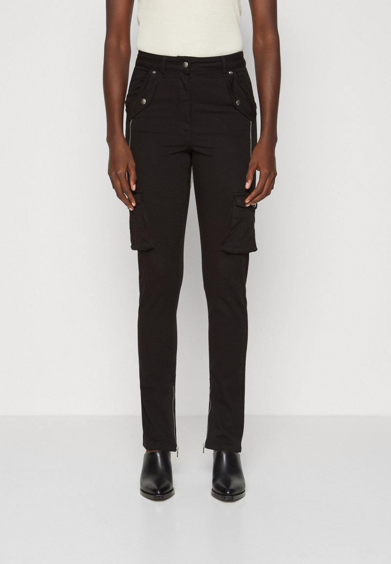 Vue de face d'une personne portant un pantalon cargo noir slim avec des détails zippés près des chevilles et des bottines noires.