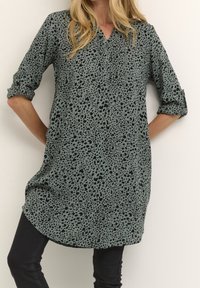 Tunique longue verte avec un motif léopard noir, dotée d'un col en V, de boutons et de manches retroussées. Tissu doux avec une coupe ample.