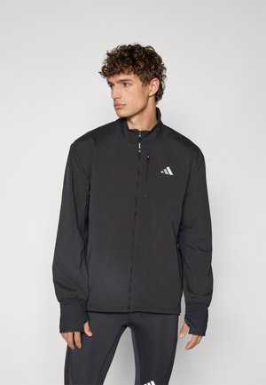 Zwarte zip-up jas met hoge kraag, elastische manchetten en subtiele Adidas-logo op de borst. Lichtgewicht, gladde stof, minimalistisch ontwerp.