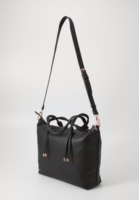 Black textured leather handbag with dual top handles and an adjustable strap. Features rose gold hardware and decorative tassels.