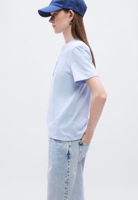 Γαλάζιο βαμβακερό μπλουζάκι με κοντά μανίκια, σε συνδυασμό με γαλάζια τζιν παντελόνια. Ένα μπλε καπέλο ολοκληρώνει το ντύσιμο, προσθέτοντας μια casual νότα.