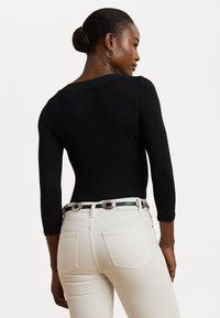 Melnas garenās piedurknes bodijai ar izgriezumu aizmugurē, savienots ar pieguļošām baltām džinsēm un melnu jostu ar sudraba akcentiem.