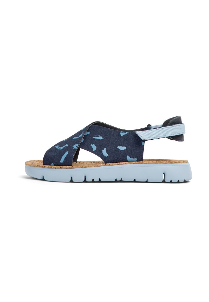 Siniset kuvioidut sandaalit korkkipohjalla, joissa on ristiligatuet ja vaaleansiniset kumipohjat. Säädettävä kantaremmi takaa tukevan istuvuuden.
