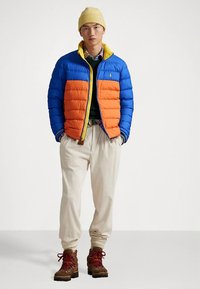 Lagana jakna sastavljena od plavog gornjeg i narančastog donjeg dijela, s žutim ovratnikom. U kombinaciji s kremastim manžetnim hlačama i smeđim planinarskim čizmama.