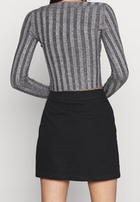 Mujer vistiendo una blusa de rayas verticales gris y negra de manga larga y una falda mini negra de cintura alta, de pie con las manos en las caderas.