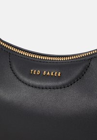 Bolso de mano de cuero negro con herrajes dorados y cierre de cremallera. Presenta el nombre de la marca en relieve, textura suave y un diseño elegante y redondeado.