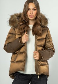 Hnědá prošívaná bunda s odnímatelnou kapucí z kožešiny, zapínáním na zip a žebrovanými manžetami. Materiál má lesklý povrch.