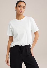 T-shirt en coton blanc avec un col rond et des manches courtes, associé à un pantalon noir à cordon de serrage. Texture lisse, coupe décontractée.