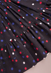 Svart tyg med röda, blå och vita solida och konturerade prickar, med rynkade, tvåskiktade volanger.