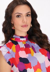 Bluză colorată cu mâneci volan. Are modele abstracte în roz, roșu, mov și galben pe un fundal deschis.