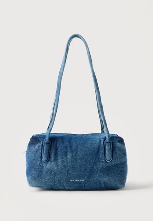 Bolso de hombro de mezclilla azul con correas largas y pequeño logo "CPH STUDIOS" en el frente sobre un fondo claro y liso.