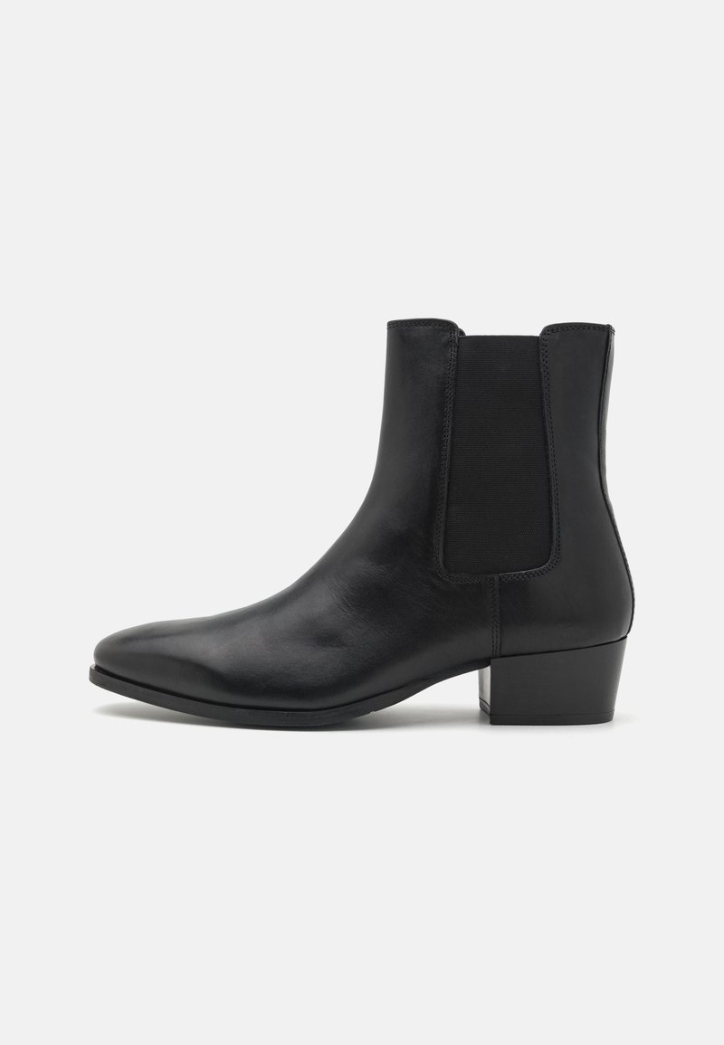 Bottine en cuir noir avec un petit talon bloc, un panneau latéral élastique, un bout pointu et une finition lisse.