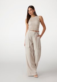 Top court beige clair avec des détails de fronces texturées, associé à un pantalon cargo beige clair ample et taille haute avec poches latérales.
