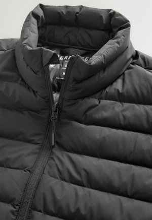 Melnā puffer jaka ar augstu apkakli, izšūtu dizainu un priekšējo rāvējslēdzēju. Gluda tekstūra ar melniem metāla detaļām.