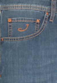 Jeans in denim con una finitura blu sbiadita. Presentano cuciture arancioni e un piccolo design della tasca con un accento ricamato stilizzato a forma di 'J'.