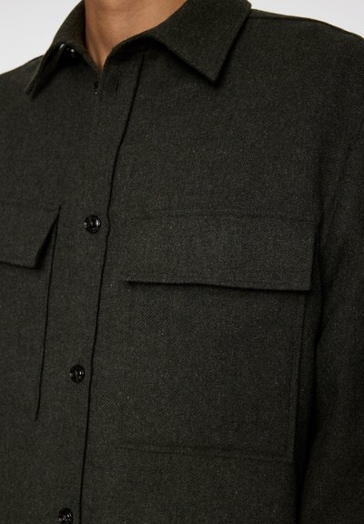 Mörkgrön ylle skjortjacka med klassisk krage, två bröstfickor och svarta knappar, med ett mjukt, texturerat tyg.