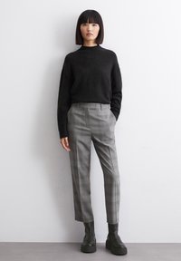 Pulover negru din tricot, pantaloni gri cu carouri și cizme cu platformă negre. Puloverul are un guler înalt; pantalonii au buzunare frontale și o croială ajustată.