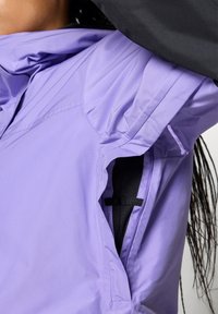 Violetinis lengvas švarkas su struktūrizuotu apykakle, užtrauktukais ventiliacijai ir juoda pamušalu. Yra raukšlės ir akcentiniai siuvinėjimai.