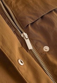 Primer plano de chaqueta de tela marrón con cremallera metálica plateada y botones a presión.