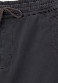 Pantalon en tissu noir avec taille élastique et cordon de serrage, doté de poches latérales et de détails de couture visibles.