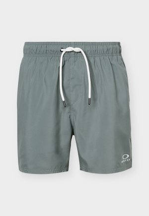 Szare spodenki kąpielowe z elastycznym pasem, białym sznurkiem do regulacji i małym logo Oakley na dolnej prawej nodze.