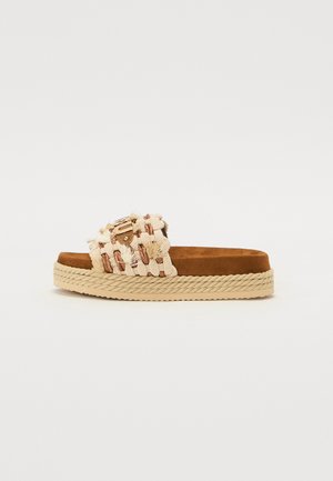 Woven beige sandals with a braided jute sole and soft brown footbed. Features decorative fringe and a gold-tone buckle accent.