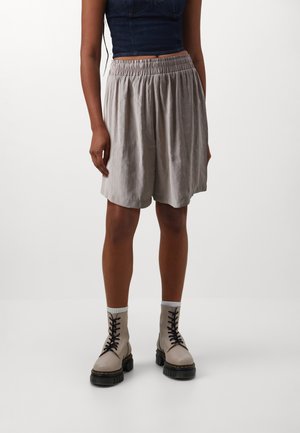 Lichtgrijze, knielange shorts met een elastische tailleband, gecombineerd met crèmekleurige veterschoenen tot de enkel met een chunky zool.