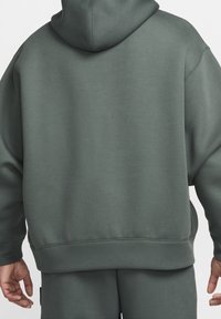 Tmavě zelená mikina s volným střihem, se stahovací kapucí, žebrovanými manžetami a lemem, vyrobená z měkké, hladké látky.