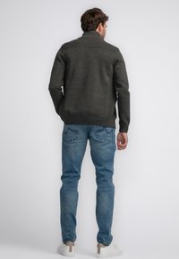 Mörkgrön sweater med ribbad krage och axeldesign, kombinerad med ljusblå jeans och vita sneakers. Bakifrån visar enkelhet och passform.