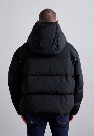 Schwarze Daunenjacke mit einer großen Kapuze, gestepptem Design und elastischen Bündchen. Getragen mit blauen Jeans, die eine lockere Passform und einen kuscheligen Stoff zeigen.