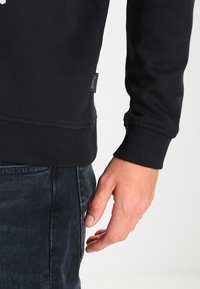 Sweatshirt nero in materiale morbido con polsini e orlo a costine. Presenta un piccolo etichetta del marchio sul lato e una vestibilità comoda.