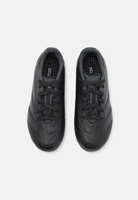 Zapatos de fútbol negros con una superficie texturizada, que cuentan con cordones, un collar acolchado y una plantilla perforada, diseñados para el rendimiento y el agarre.
