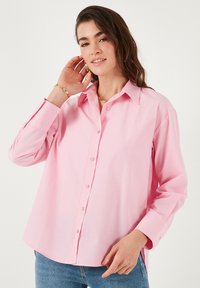 Light pink button-up shirt with a classic collar and long sleeves, featuring a relaxed fit and smooth cotton texture.