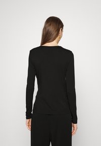 Czarny długi rękaw top w miękkim materiale z okrągłym dekoltem, charakteryzujący się dopasowanym kształtem i minimalistycznym designem, noszony z dopasowanymi czarnymi spodniami.