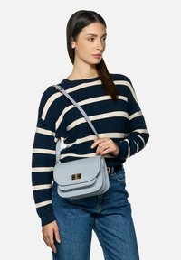 Bolso cruzado de cuero en color azul claro, con cierre de solapa y herrajes dorados. El bolso tiene una forma estructurada y una textura suave.