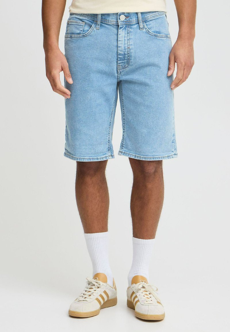 Lys blå denimshorts med rett snitt, frontlommer og oppbrettede kanter. Kombinert med hvite sokker og beige treningssko.