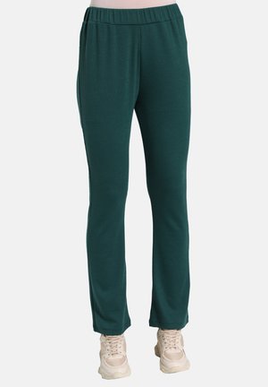 Teal ribbed trousers feature an elastic waistband, a relaxed fit, and a straight leg design, paired with light-colored sneakers.