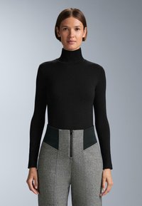 Čierny rolák s dlhými rukávmi v kombinácii s vysokými šedými vzorovanými nohavicami s čiernymi akcentmi a predným zipsom.