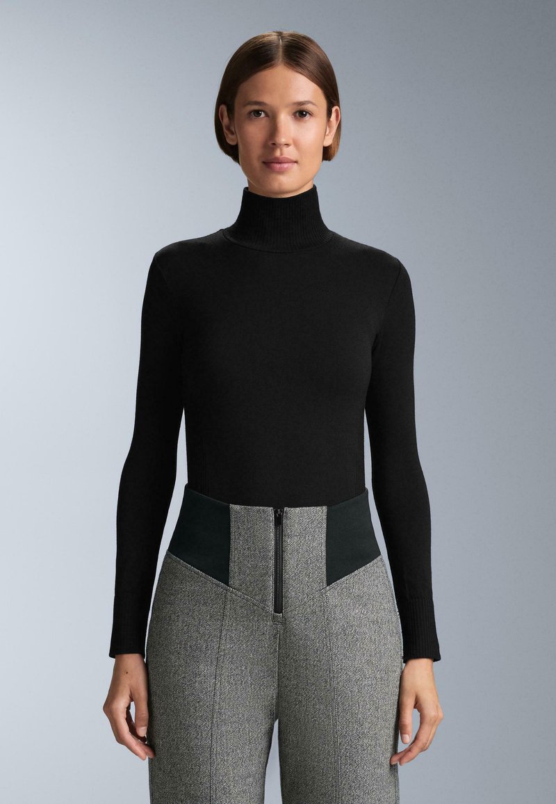 Čierny rolák s dlhými rukávmi v kombinácii s vysokými šedými vzorovanými nohavicami s čiernymi akcentmi a predným zipsom.