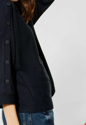 Dunkelblauer Pullover mit strukturiertem Finish, mit großen schwarzen Knöpfen an der Seite und dreiviertel Ärmeln.