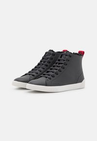 Hoge sneakers van gestructureerd zwart leer met een witte rubberen zool, voorzien van een rode accent bij de hak en zwarte veters.