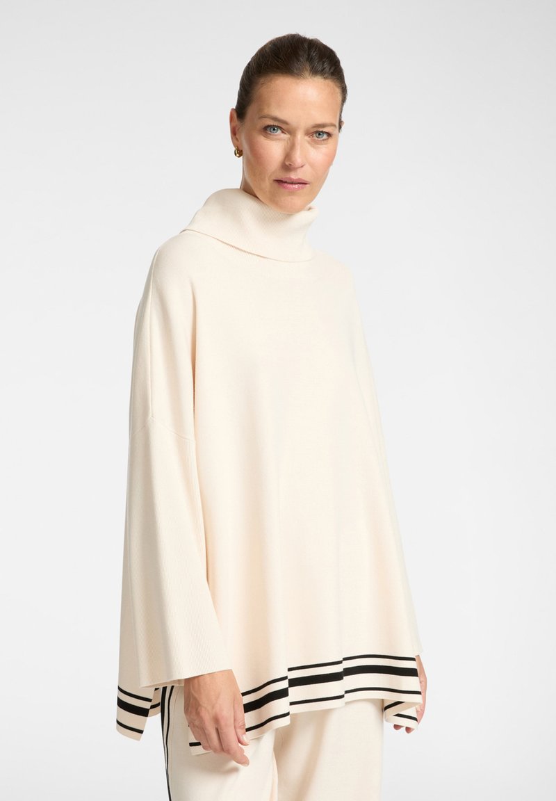 Jersey de cuello alto color crema con mangas anchas, que presenta un dobladillo a rayas negras. Fabricado con material suave, tiene un ajuste holgado y oversized.