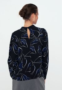 Blusa nera con motivi a foglia bianchi e blu, con maniche lunghe, schiena a occhiello e texture del tessuto per una leggera caduta.