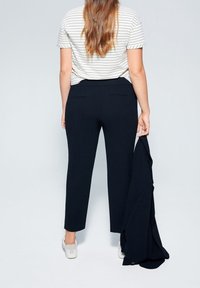 Granatowe spodnie o dopasowanym kroju, z dwoma tylnymi kieszeniami, zestawione z pasiastym topem z krótkim rękawem i białymi tenisówkami.