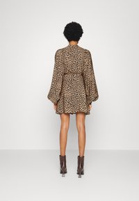 Kleid mit Leopardenmuster, langen, voluminösen Ärmeln, tailliertem Schnitt, ausgestelltem Rock und glattem Stoff. Braune, hohe Knöchelstiefel runden das Outfit ab.