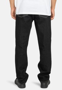 Jeans de denim negro con corte recto, bolsillos traseros y acentos de costura blanca. La textura es suave con un acabado clásico.
