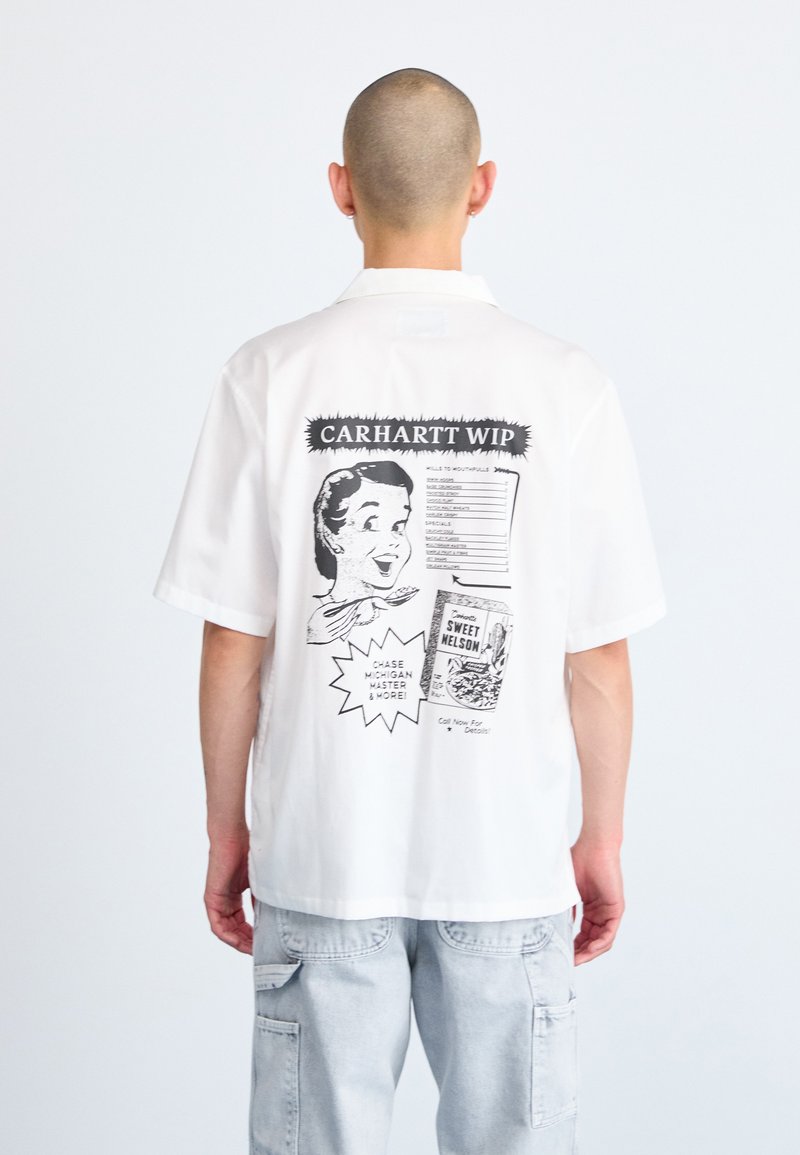Camisa blanca de manga corta con un diseño gráfico en la parte posterior que incluye texto negro e ilustraciones. Corte relajado con cuello y dobladillo recto.