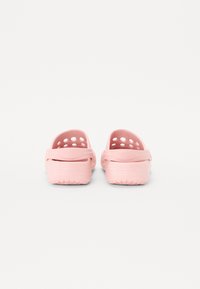 Pink clogs made of flexible material, featuring drainage holes, rear strap, and textured sole for grip. Smooth finish with rounded shape.