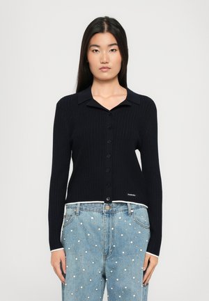 Navy ribbed cardigan with a button-up front, featuring a collar, long sleeves, and a white accent at the hem. Brand name displayed at the side.